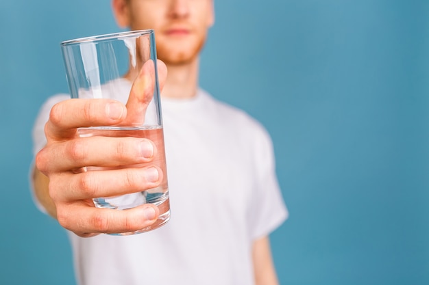 un joven pelirrojo con una camiseta blanca bebiendo agua de un vaso.