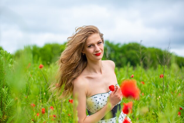 Una joven de pelo largo disfruta de los colores de la naturaleza en un campo de amapolas en flor en un caluroso día de verano.