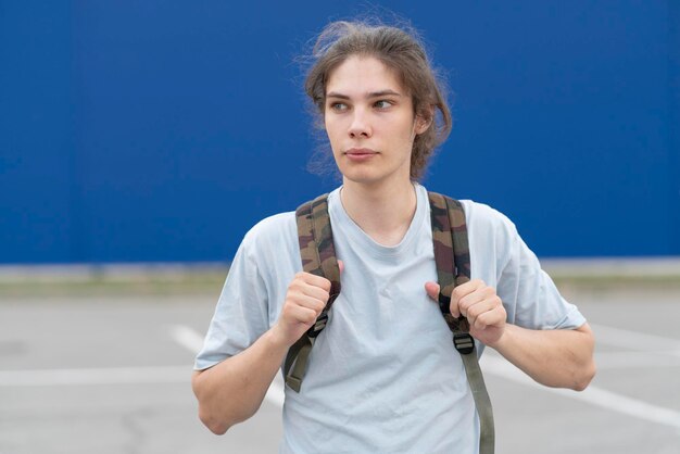 Un joven con el pelo largo parado al aire libre con una mochila