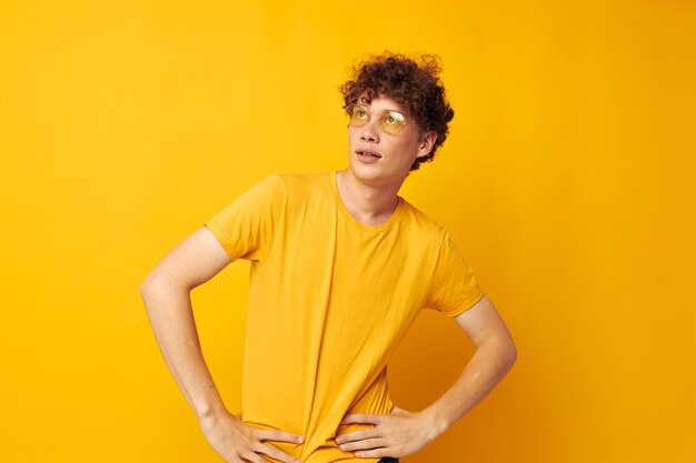 Joven de pelo rizado con gafas elegantes camiseta amarilla posando fondo aislado inalterado