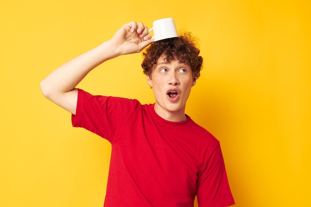 Joven de pelo rizado posando con una taza blanca y en manos de una bebida de fondo amarillo inalterado