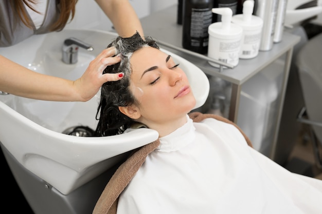 Joven peluquera lava su cabello con champú y masajea la cabeza de una joven en un moderno salón de peluquería