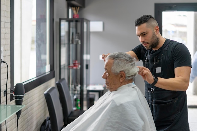 Joven peluquero cortando el cabello de un anciano con tijeras