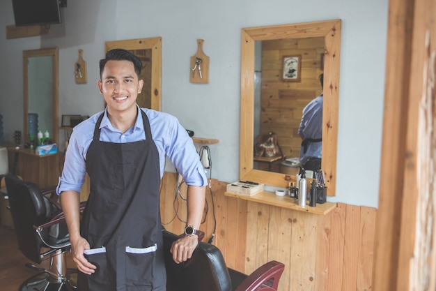 Joven peluquero experto smilin mirando a la cámara en la barbería