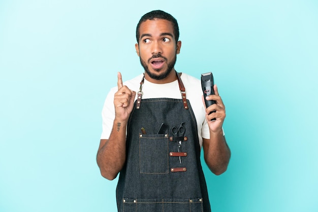 Joven peluquero latino aislado de fondo azul pensando en una idea apuntando con el dedo hacia arriba