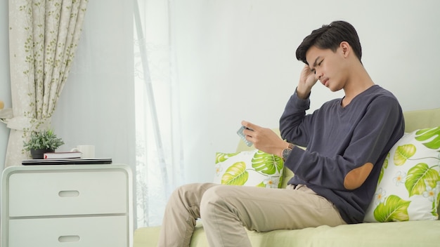 Joven pensando en jugar juegos en el teléfono inteligente en casa