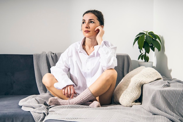 Foto una joven pensativa con camisa blanca y calcetines sentada en el sofá