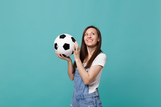 Una joven pensativa fanática del fútbol apoya al equipo favorito con una pelota de fútbol mirando hacia arriba aislada en un fondo azul turquesa. Emociones de la gente, concepto de estilo de vida de ocio familiar deportivo. Simulacros de espacio de copia.