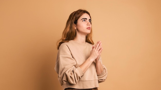 Una joven pensativa orando a Dios en un estudio marrón.