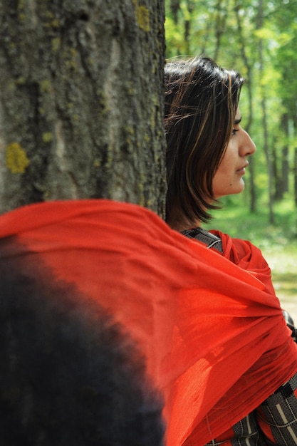 Foto una joven pensativa de pie junto al tronco de un árbol en el bosque