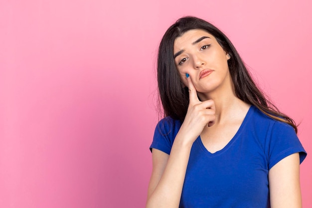 Una joven pensativa le puso el dedo a la chica y se puso de pie sobre un fondo rosa