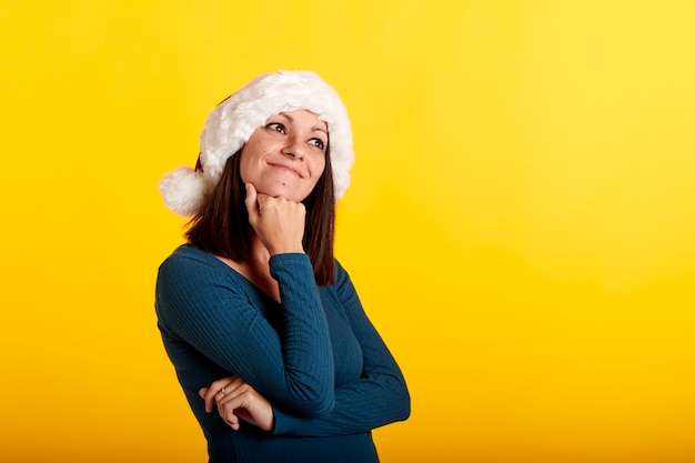 Una joven pensativa con un sombrero de Santa Claus con un fondo amarillo