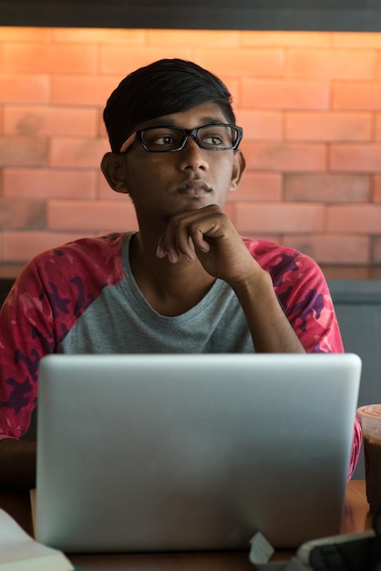 Un joven pensativo con una computadora portátil estudiando en un café.