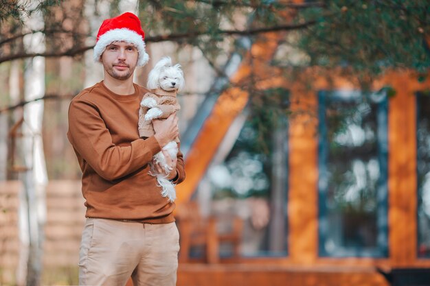 Joven con perro pequeño en fondo de casa de sombrero de santa