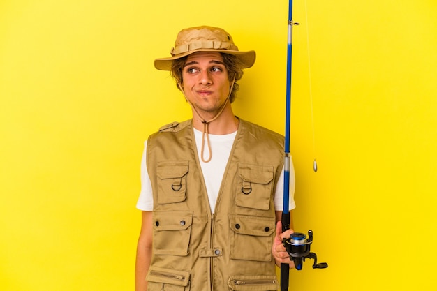 Joven pescador con maquillaje con varilla aislado sobre fondo amarillo confundido, se siente dudoso e inseguro.