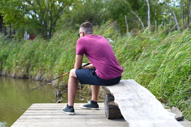 Joven pescador sentado en el muelle de madera pescando en el lago