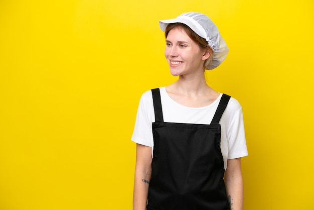 Joven pescadora inglesa aislada de fondo amarillo mirando al costado y sonriendo