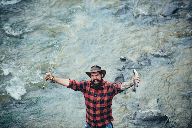 Joven pescando Pescador con carrete giratorio de caña en la orilla del río Hombre atrapando peces tirando de la caña mientras pesca en el lago Naturaleza salvaje Emocionado pescador asombrado en el agua atrapando truchas vista superior