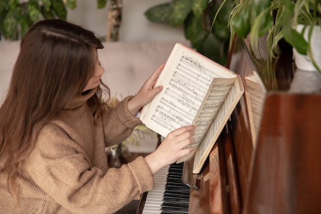 Una joven pianista con un acogedor suéter se sienta al piano y hojea una colección de notas.