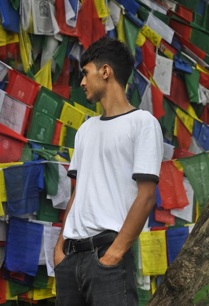 Foto un joven de pie afuera mirando hacia los lados con banderas de oración budista en el fondo