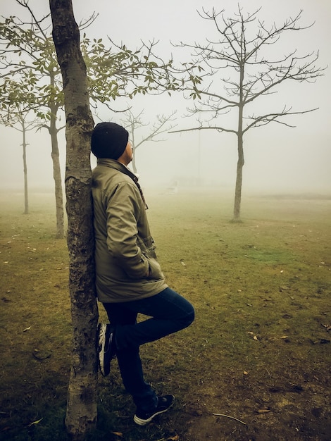 Un joven de pie apoyado en un árbol