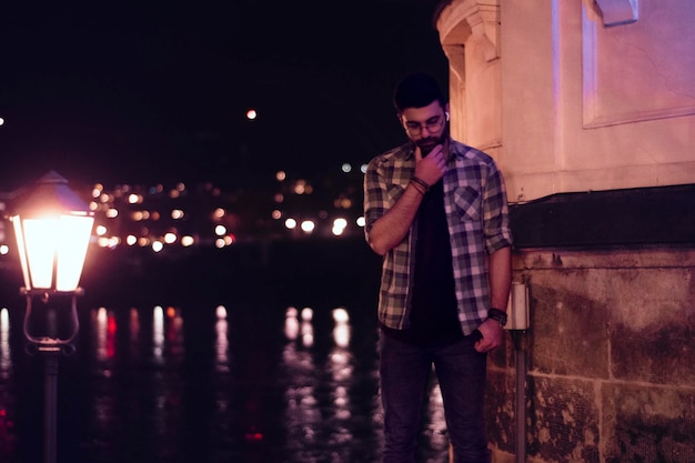 Foto joven de pie contra una pared iluminada por la noche