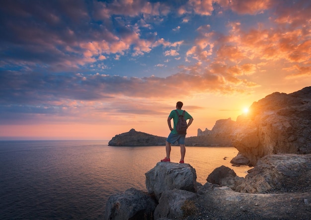 Joven de pie con mochila en la piedra al atardecer