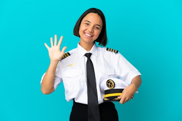 Joven piloto de avión sobre fondo azul aislado contando cinco con los dedos
