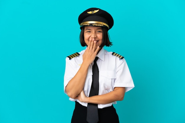 Joven piloto de avión sobre fondo azul aislado feliz y sonriente cubriendo la boca con la mano