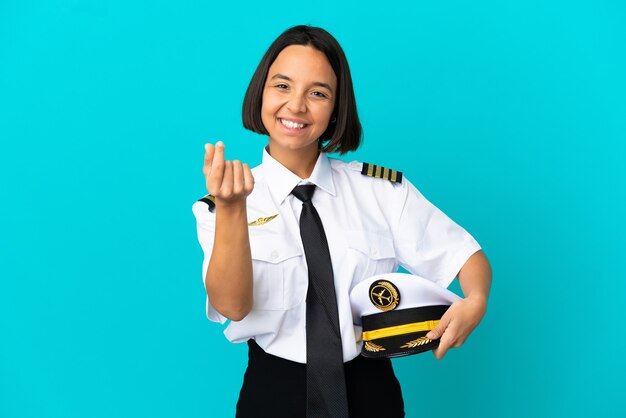 Joven piloto de avión sobre fondo azul aislado haciendo gesto de dinero