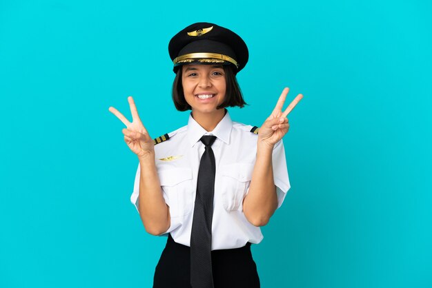 Joven piloto de avión sobre fondo azul aislado mostrando el signo de la victoria con ambas manos