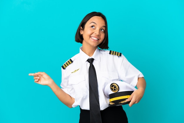 Joven piloto de avión sobre fondo azul aislado que señala con el dedo a los laterales y feliz