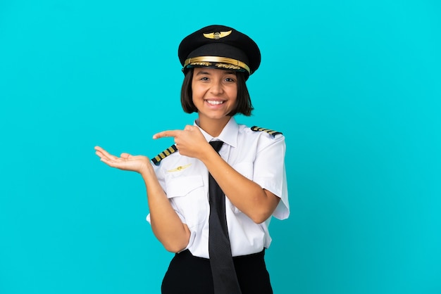 Joven piloto de avión sobre fondo azul aislado sosteniendo copyspace imaginario en la palma para insertar un anuncio