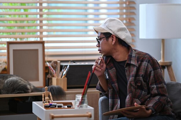 Joven pintando un cuadro en la sala de estar y jugando con su gato.