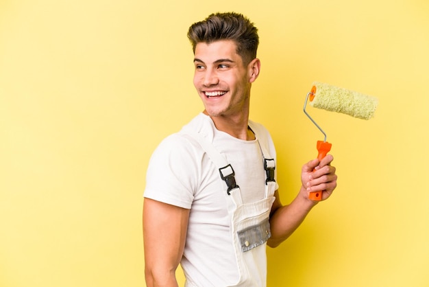 El joven pintor aislado de fondo amarillo mira a un lado sonriendo alegre y agradable