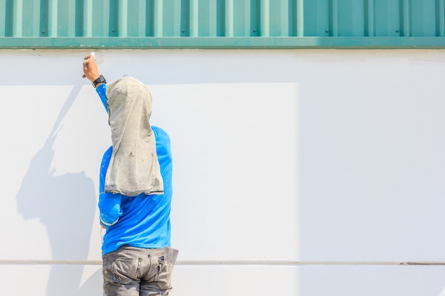 Joven pintor pintando una pared con pinceles