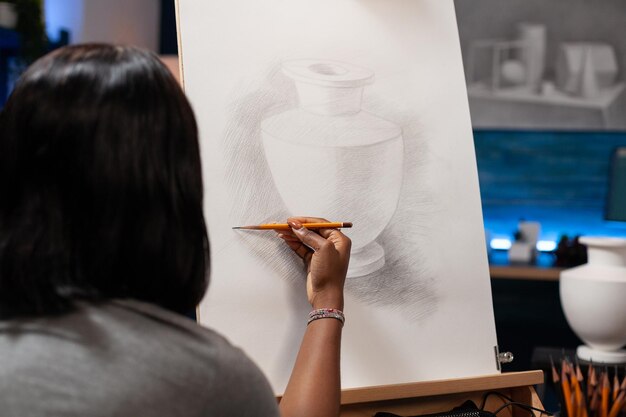 Joven pintor en silla de ruedas dibujando ilustraciones de jarrones usando lápiz gráfico durante la lección de pintura en el estudio de creatividad. Estudiante de artista con discapacidad dibujando sobre lienzo. Concepto de pinturas