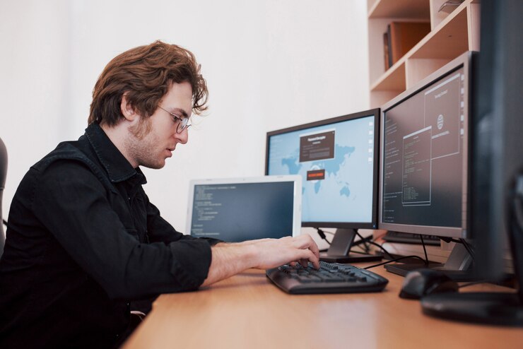 Foto el joven pirata informático peligroso desglosa los servicios gubernamentales al descargar datos confidenciales y activar virus. un hombre usa una computadora portátil con muchos monitores