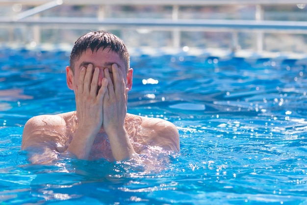 Joven en la piscina con la cara cubierta con las manos