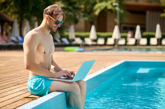 Joven en la piscina trabajando en una laptop