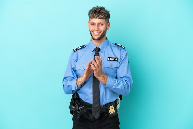 Joven policía rubio aislado blanco sobre fondo azul aplaudiendo después de la presentación en una conferencia