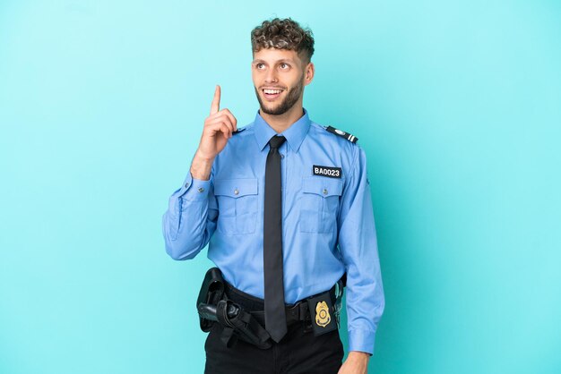 Joven policía rubio aislado blanco sobre fondo azul apuntando hacia arriba y sorprendido