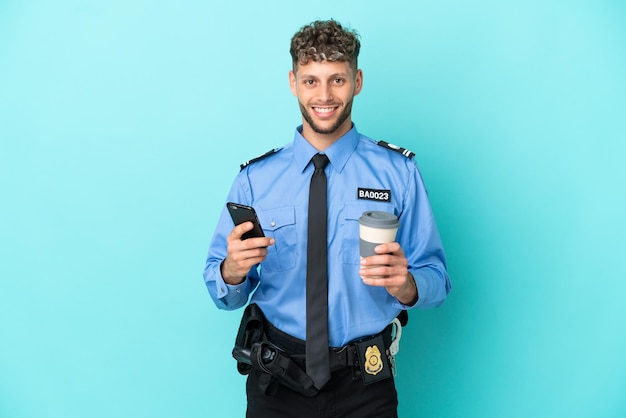 Joven policía rubio aislado blanco sobre fondo azul con café para llevar y un móvil