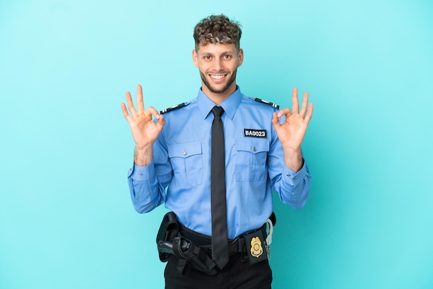 Joven policía rubio hombre aislado blanco sobre fondo azul mostrando un signo de ok con los dedos