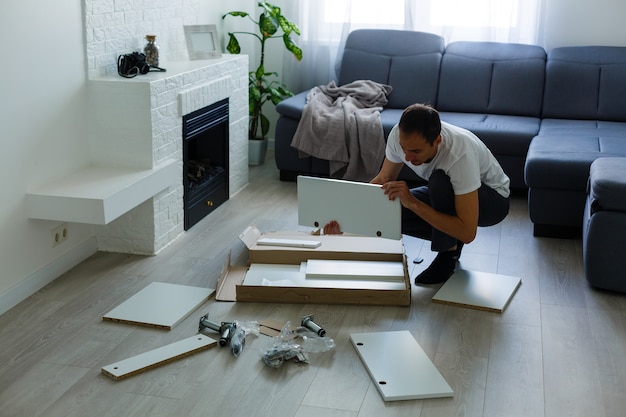 joven poniendo muebles de autoensamblaje mientras se mudan a su nueva casa.