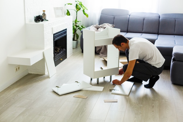 joven poniendo muebles de autoensamblaje mientras se mudan a su nueva casa.