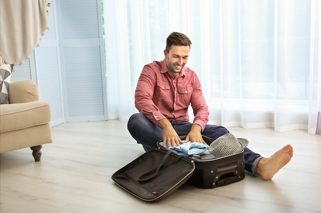 Joven poniendo la ropa en la maleta en el piso