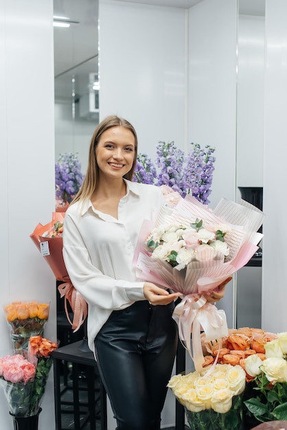 Una joven posa con un hermoso ramo festivo en el contexto de una acogedora florería Floristería y elaboración de ramos en una floristería Pequeña empresa