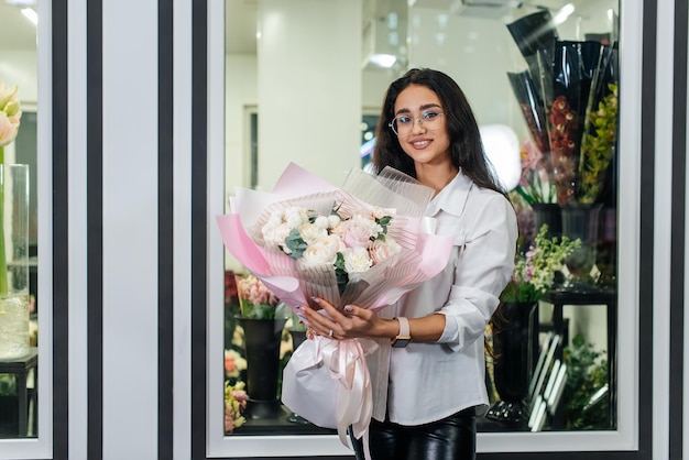 Una joven posa con un hermoso ramo festivo en el contexto de una acogedora florería Floristería y elaboración de ramos en una floristería Pequeña empresa