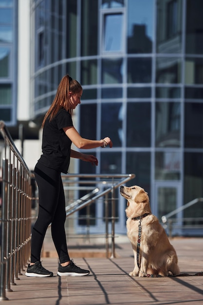 Una joven positiva se divierte y hace trucos con su perro cuando camina al aire libre cerca del edificio comercial